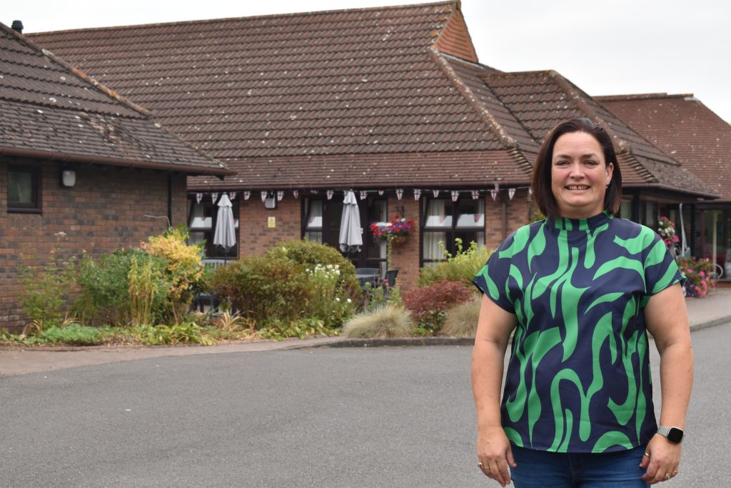Pippa Curtin standing outside of Lindsey Lodge Hospice in a green and blue top and jeans