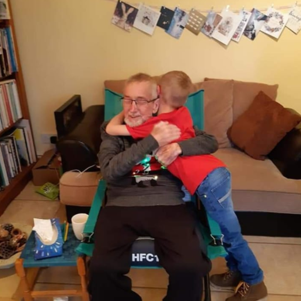 Glyn sits in a chair and hugs his grandson on christmas day.