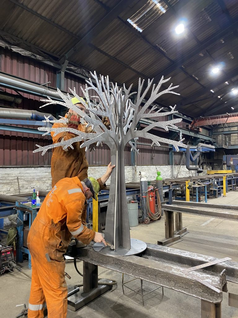Lindsey Lodge Memorial tree during construction at SC4. Image shows metal tree on a bench with with metal workers.